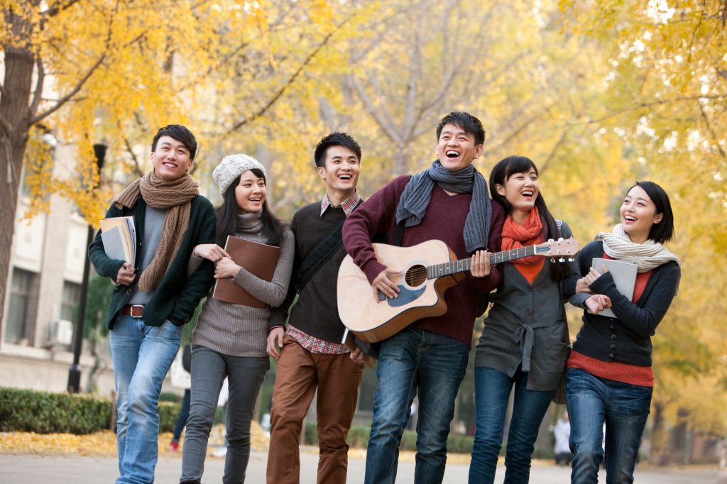 College students walking and playing guitar on campus in autumn
