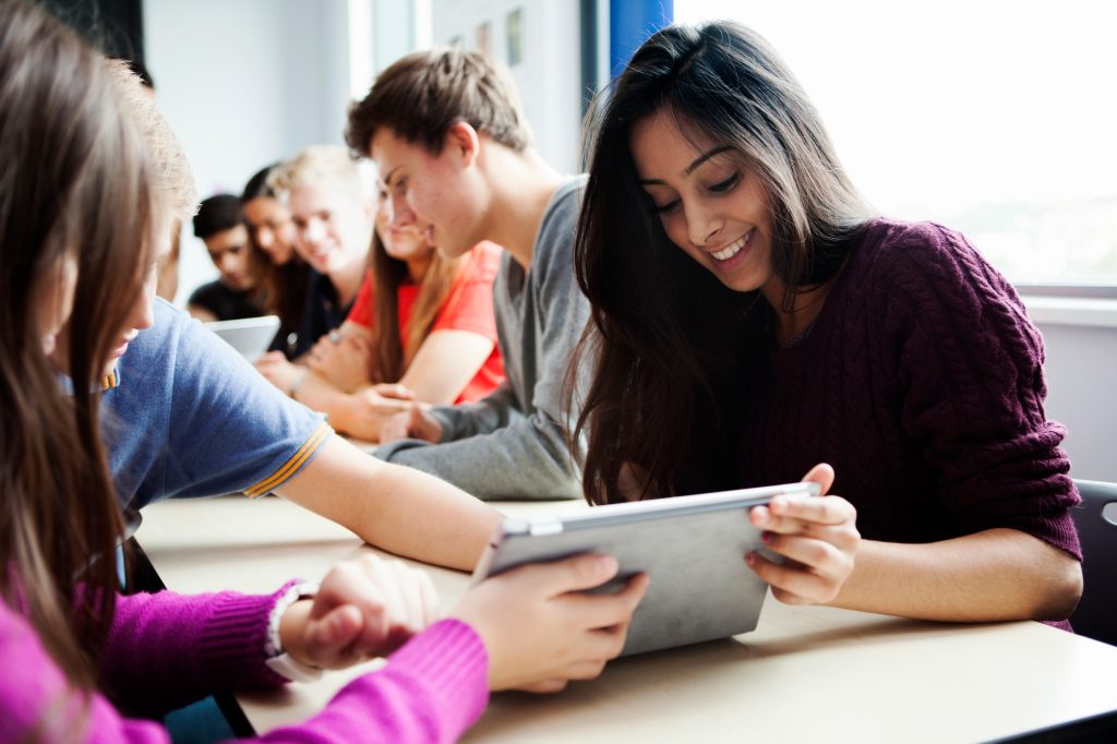 Teenage schoolgirls sitting at desk using digital tablet